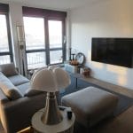 Salon rénové avec téléviseur sur support mural et une belle lumière apportée par les larges baies vitrées - Rénovation d'un appartement à Nancy